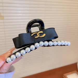 Détail d'une grande pince à cheveux noire avec perles blanches et nœud en satin à boucle dorée