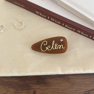Close-up of brown acetate teardrop hair clip with golden letters and a crystal