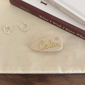 Detail of beige matte acetate hair clip with gold lettering and sparkling rhinestone