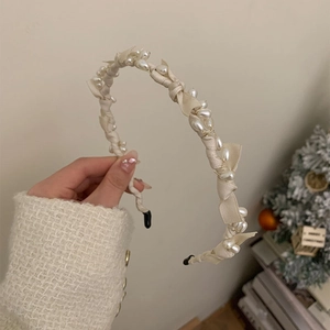Close-up of elegant cream headband featuring delicate pearls and bow details held by hand
