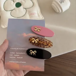Three-piece set of oval hair clips with gold bow accents in pink, leopard, and black