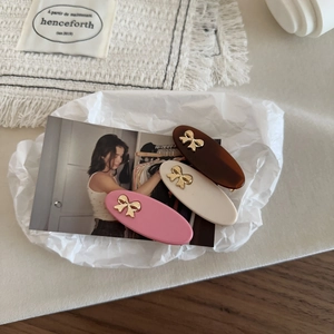 Three oval resin hair clips in brown, white, and pink with golden metal bow accents