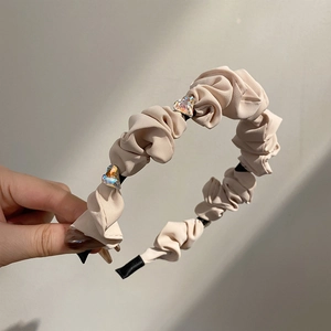 Detail of beige pleated fabric headband featuring three sparkling crystal heart accents