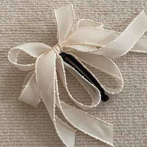 Detailed view of cream bow banana hair clip with textured ribbon and layered design
