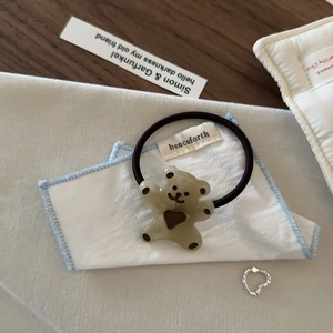 Détail d'un ours en résine verte avec cœur sur un élastique à cheveux marron