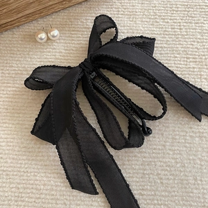 Detail of a black ribbon bow banana clip with semi-transparent texture on a beige carpet