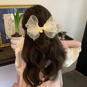 Detail of elegant cream organza bow hair clip with pearl center on a woman hair