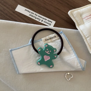 Détail de l'élastique ours vert et de la bague coeur argentée sur un tissu blanc doux