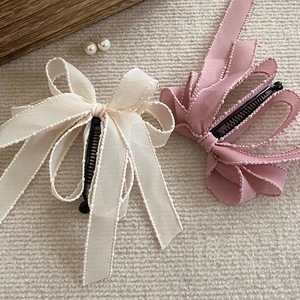 Detail of multi-layered bow hair clips with bead-edged ribbons in beige and purple