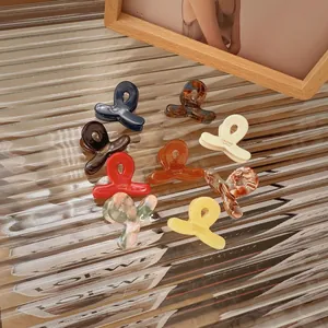 Set of 9 colorful acetate mini hair claw clips arranged on elegant textured glass