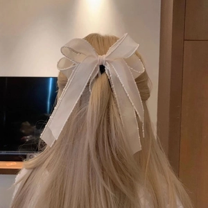 Detail of a large cream ribbon bow hair clip with wavy edges on blonde hair