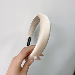 Detailed view of cream satin padded headband with single pearl and handmade label