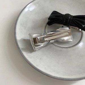 Détail de barrettes à cheveux nuds en cuir noir et métal argenté avec base bec de canard