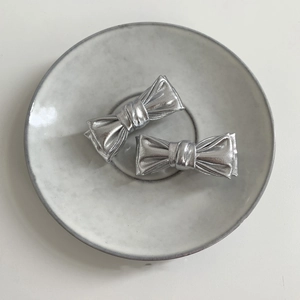 Détail de deux barrettes noeuds argentées sur une assiette, texture métallique chic