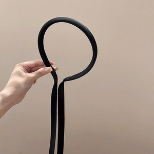 Détail d'un serre-tête fin en satin noir avec de longs rubans tenu à la main