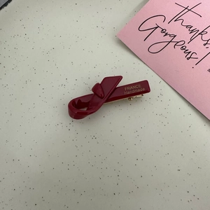 Detailed macro view of a handmade burgundy satin bow hair clip with gold logo
