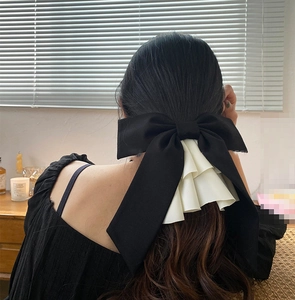 Detail of oversized black satin bow hair clip with white pleated ruffles on long hair