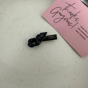 Detail of a black glossy resin twist bow hair clip featuring gold France Handmade lettering