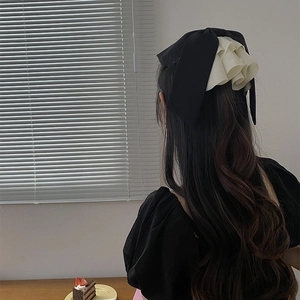 Oversized satin bow hair clip with white ruffle trim shown from the back on long hair
