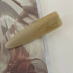 Detail of a French-style acetate hair barrette in cream color with elegant gold lettering