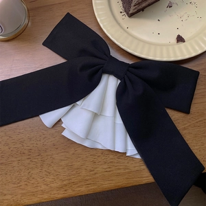 Detail of elegant black satin bow hair clip with white ruffled trim on a wooden table