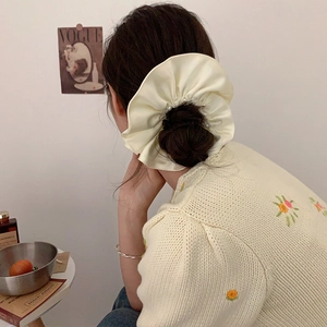 Close-up of beige satin scrunchie with pearls styled on a hair bun with floral cardigan