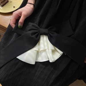 Detailed close-up of large oversized black satin bow clip with pleated white trim