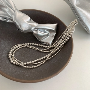 Gros plan d'un collier à plusieurs rangs de perles argentées sur une assiette texturée