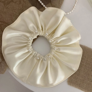 Detail shot of a cream satin scrunchie featuring elegant white pearls on a textured background