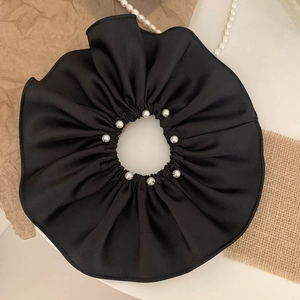 Detail of oversized black satin scrunchie with elegant pearl accents and wavy pleats