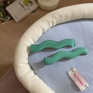Detail of two green wavy acrylic hair clips with a smooth finish on a soft fabric background