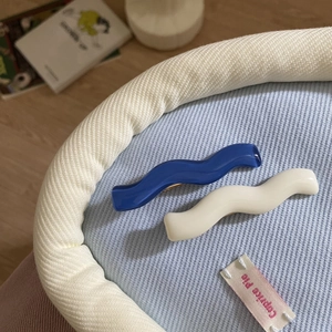 Detail view of wavy blue and white resin hair clips on a soft blue knitted fabric background