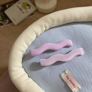 Close-up of wavy acrylic hair clips in pastel purple on a textured fabric background