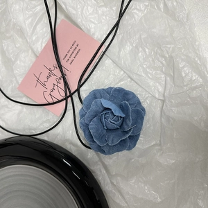 Collier choker rose camélia en denim avec cordon noir sur fond blanc texturé
