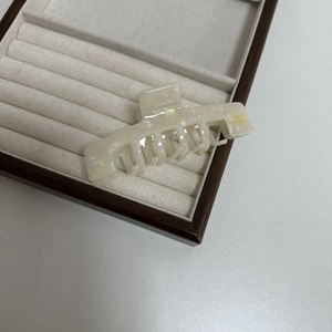 Close-up of cream acetate hair claw clip with pearlescent finish on a jewelry display tray