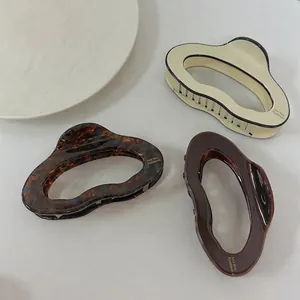 Three elegant acetate hair claws in cream, tortoiseshell and brown with wavy hollow design