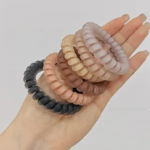 Détail de cinq élastiques spirales mats aux couleurs gelée tenus à la main
