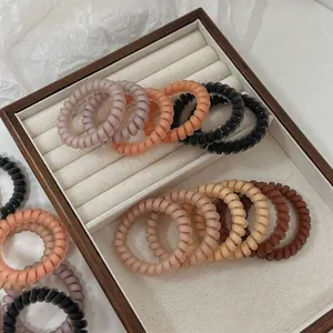 Lot d'élastiques spirale mats aux couleurs Morandi présentés sur un plateau en bois