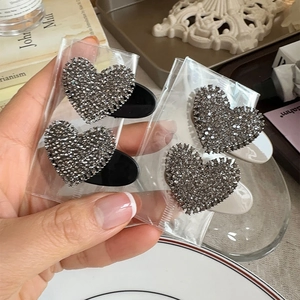 Set of four heart-shaped hair clips with dark grey rhinestones on an elegant background