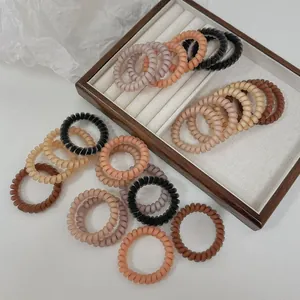 Gros plan d'élastiques à cheveux spirales mats aux tons terre sur fond blanc texturé