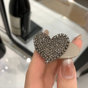 Detailed close-up of a heart-shaped hair clip with dark grey rhinestones on an oval base