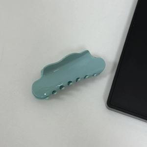Detail of light blue acetic acid hair claw clip with wave edges on a white surface