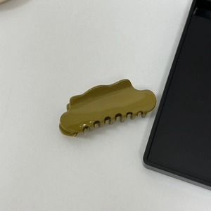 Detail view of an olive green cloud acetate hair claw clip with wave edges on white surface