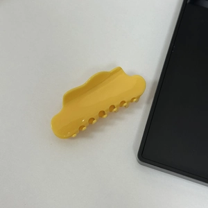Detail of a yellow cloud-shaped hair claw clip with a glossy finish and metal spring