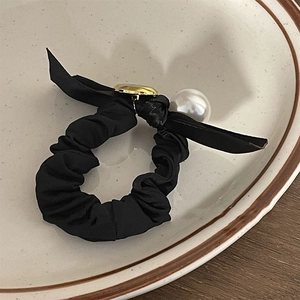 Detail of elegant black pearl bow scrunchie on ceramic dish with wooden background