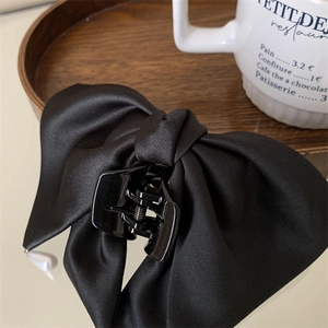 Pince à cheveux avec nœud en satin noir et pendentif perle sur plateau en bois