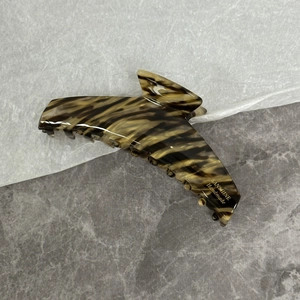 Gros plan d'une pince à cheveux en acétate avec motif écaille et logo doré gravé