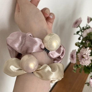 Gros plan de chouchous en satin avec grandes perles posés sur une table en bois