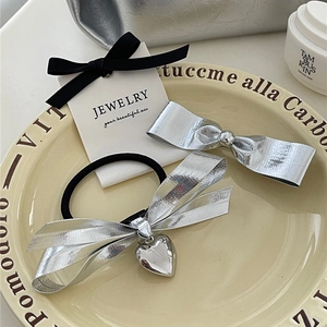 Détail de la pince à cheveux noeud argenté et chouchou avec pendentif coeur sur assiette