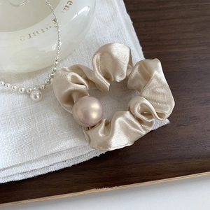 Gros plan d'un chouchou en satin champagne avec perle sur un tissu en lin blanc